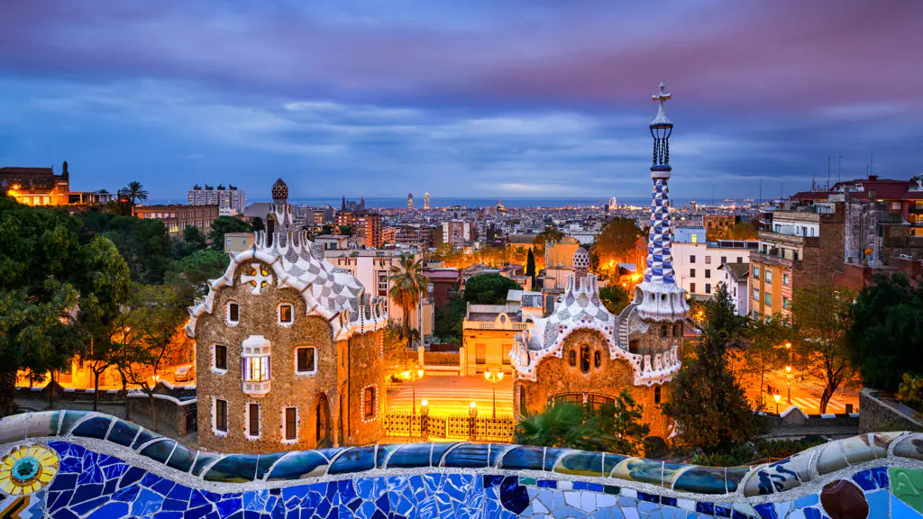 Gaudi's Park Guell glows at dusk above the Barcelona skyline, a fantastical blend of art, architecture, and nature