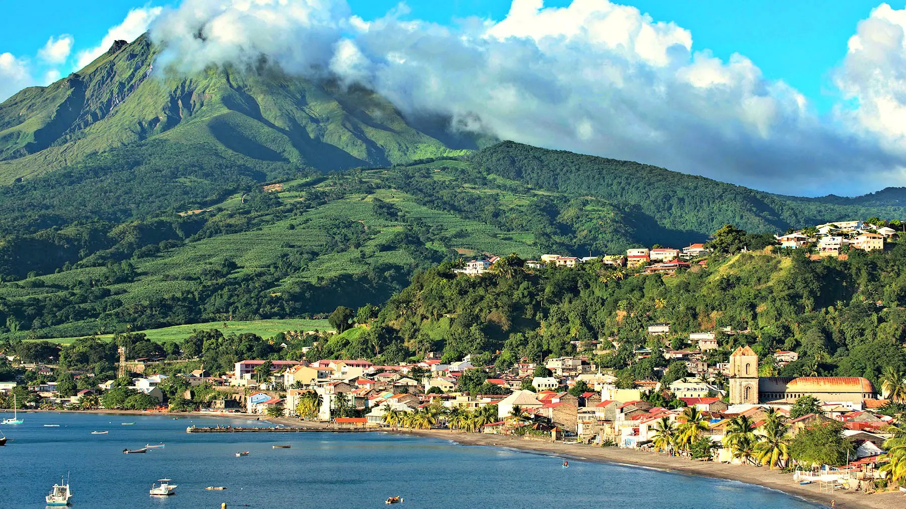 The town of Saint-Pierre curves along Martinique's black sand coastline beneath the lush volcanic slopes of Mount Pelee