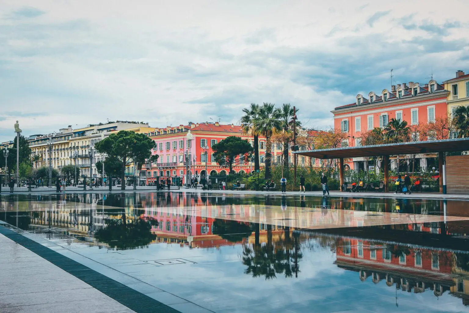 The colorful facades of Place Massena in Nice are mirrored in a reflecting pool, the gateway to the French Riviera