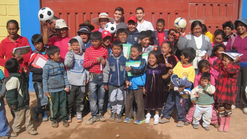 Prometour student volunteers with local Peruvian children holding soccer balls and school supplies during a community outreach visit