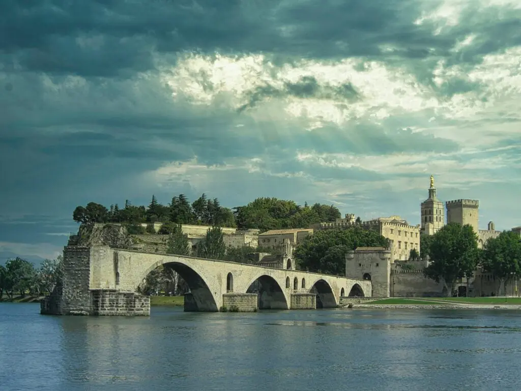 The medieval Pont Saint Benezet and Palace of the Popes in Avignon span the Rhone River under a moody stormy sky