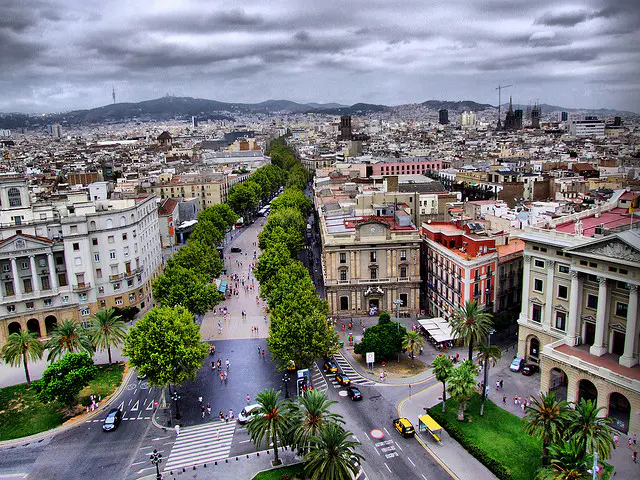 Las Ramblas stretches through the heart of Barcelona toward the Sagrada Familia and the hills beyond under a dramatic sky