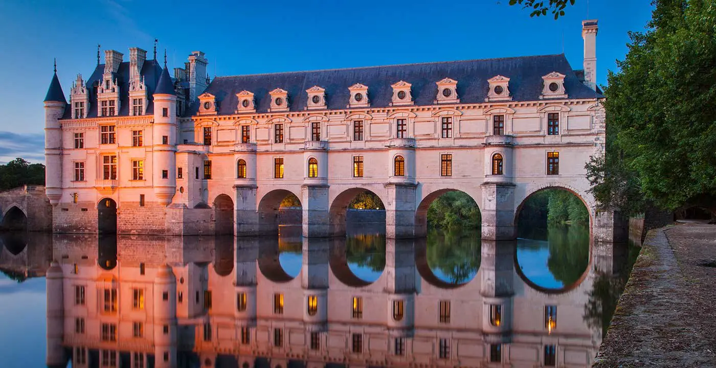Chateau Chenonceau glows at dusk above its arched bridge over the River Cher in the Loire Valley, France 