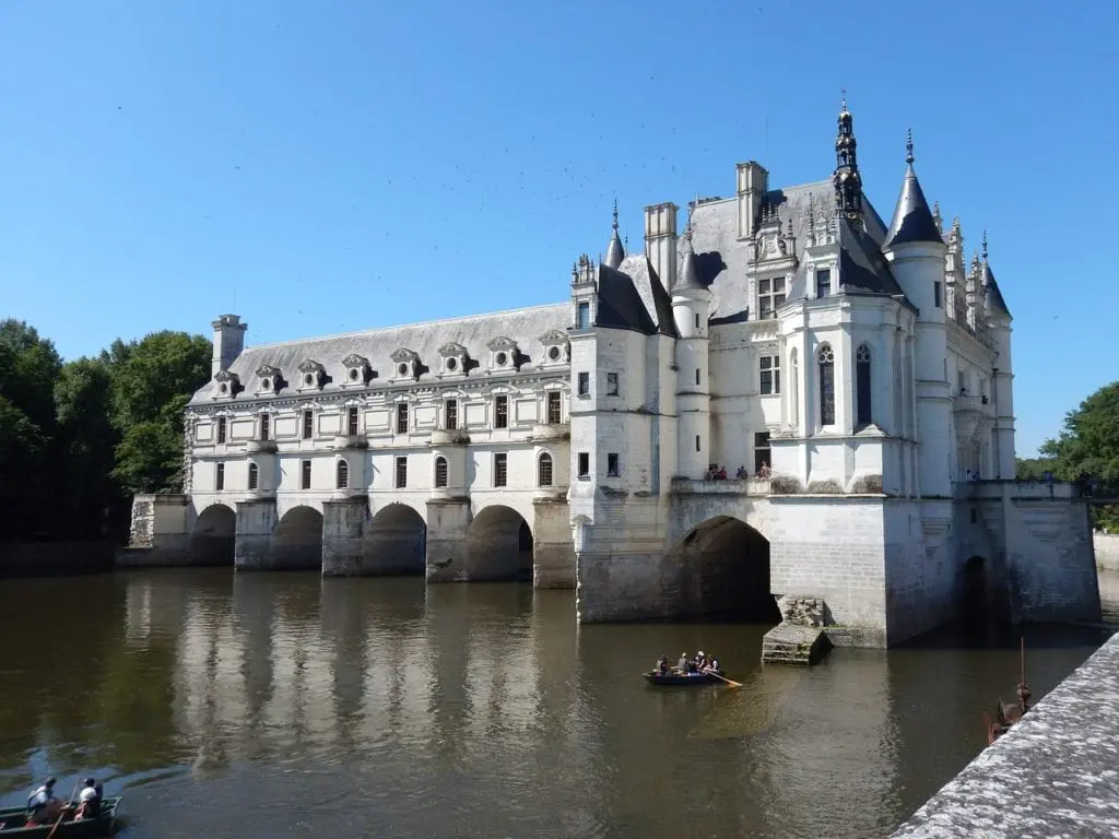 Chateau Chenonceau spans the River Cher on a summer day, with visitors rowing beneath its arches in the Loire Valley
