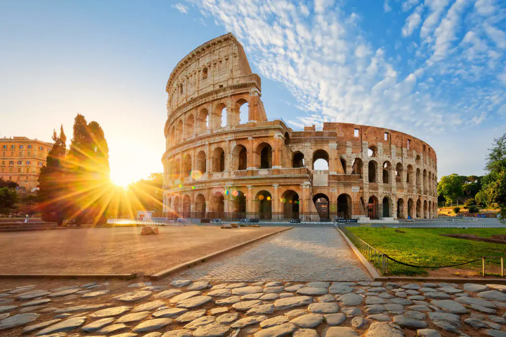 The Colosseum blazes in golden sunrise light in Rome, its ancient arches and travertine stone lit from behind in one of the city's most dramatic early morning scenes