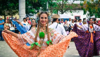 A smiling Costa Rican folkloric dancer in a traditional orange and white ruffled dress performing at an outdoor cultural festival