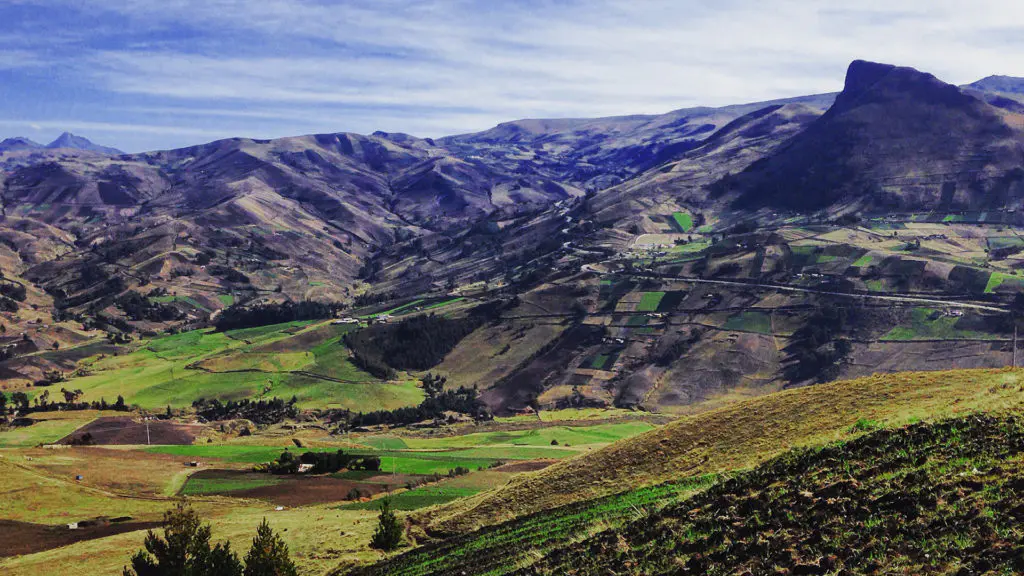 Panoramic view of the Ecuadorian Andes highlands with patchwork green farmland, deep valleys, and a flat-topped volcanic peak