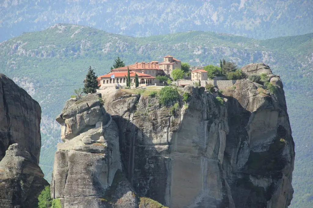 A Meteora monastery clings to its sandstone pinnacle above a wide Greek valley under brooding clouds 