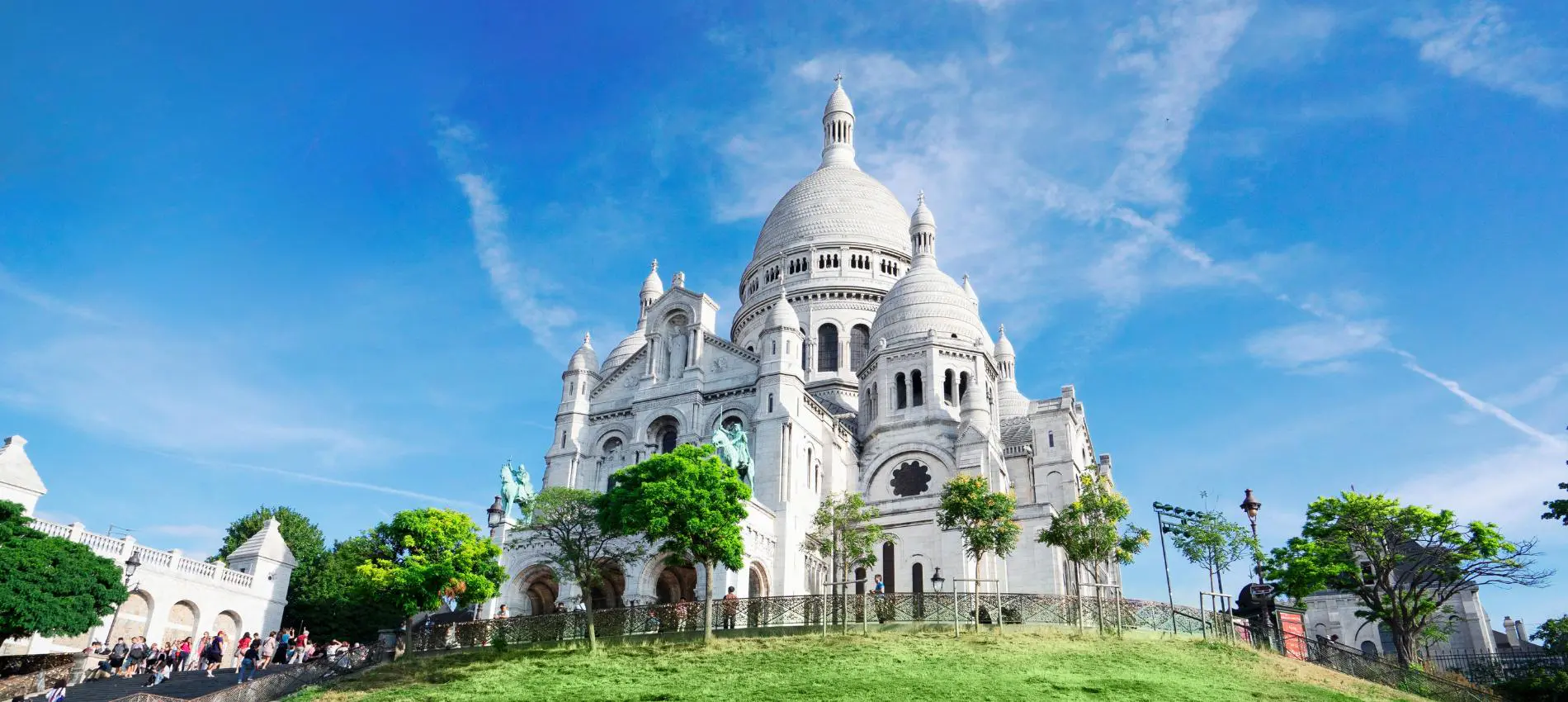 Sacre Coeur Basilica crowns the Montmartre hill in Paris, its white stone domes rising above the surrounding trees