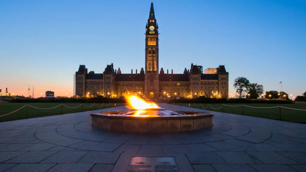 The Centennial Flame burns in front of Parliament Hill's Centre Block at dusk, a powerful symbol of Canadian unity in the heart of Ottawa