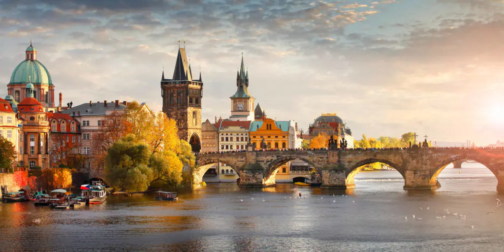 Charles Bridge glows in golden hour light above the Vltava River in Prague, with the Old Town's towers and copper domes reflected in the water below