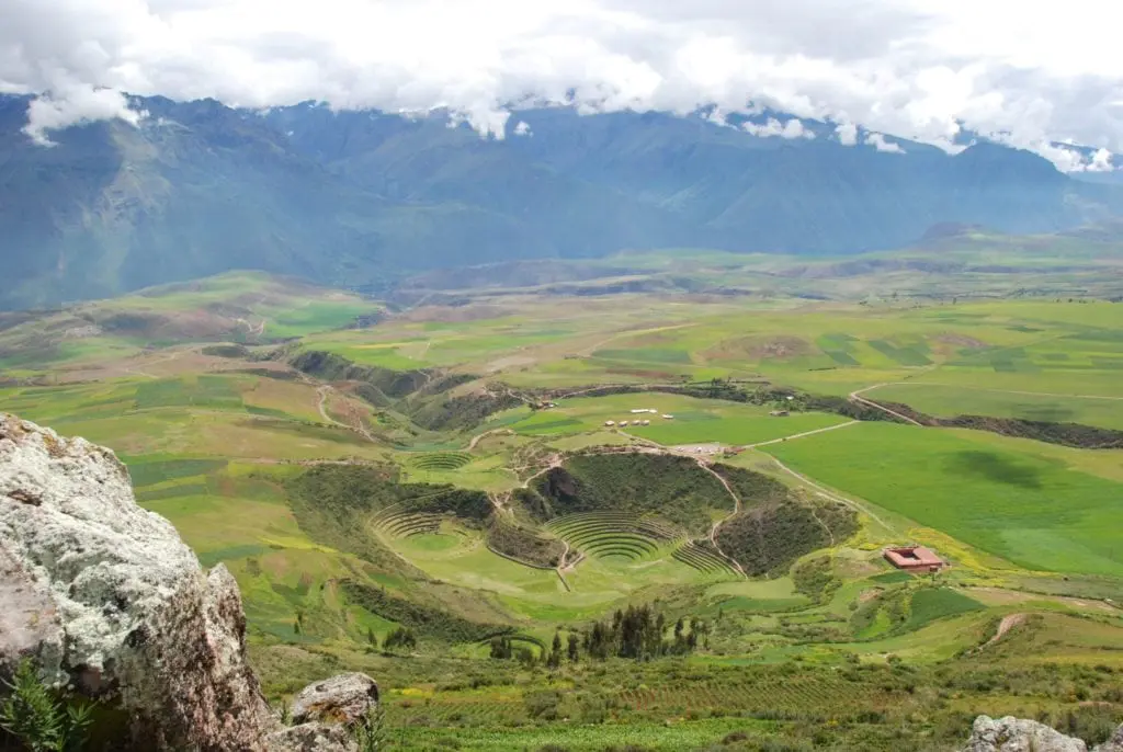 The circular Inca terraces of Moray sit within the vast green Sacred Valley of Peru, with the snow-capped Andes rising behind