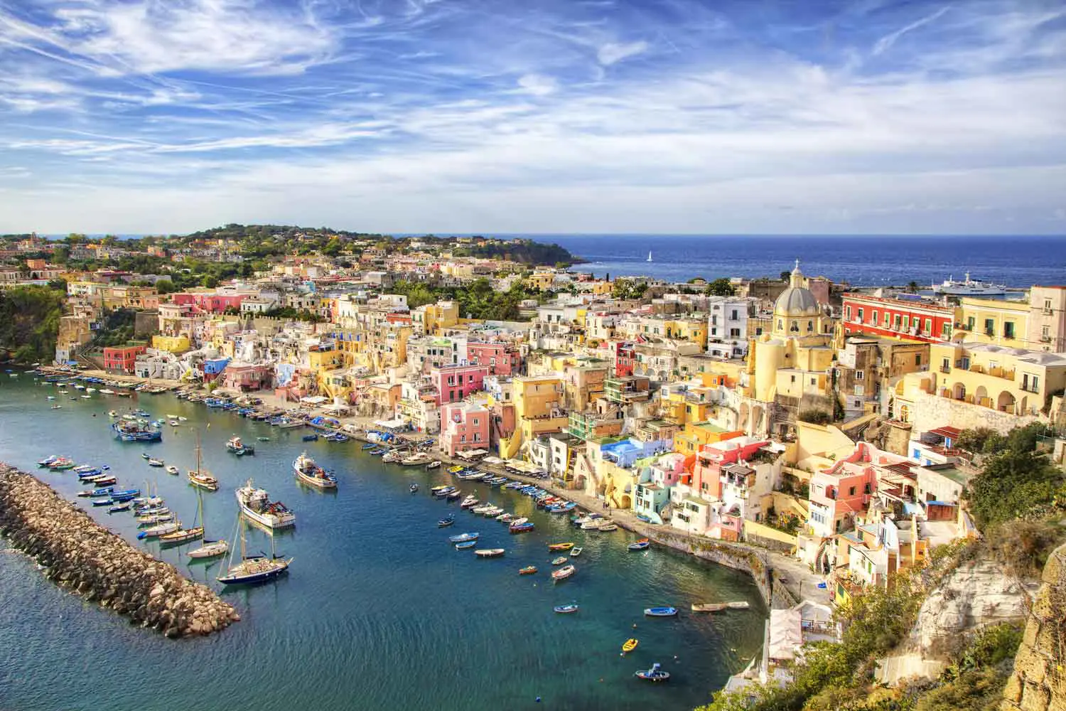 White-walled buildings cascade down a lush clifftop above the Bay of Naples, with the sparkling Tyrrhenian Sea stretching to the horizon