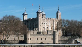 The Tower of London viewed from across the Thames, with its medieval stone walls, turrets, and the Union Jack flying above