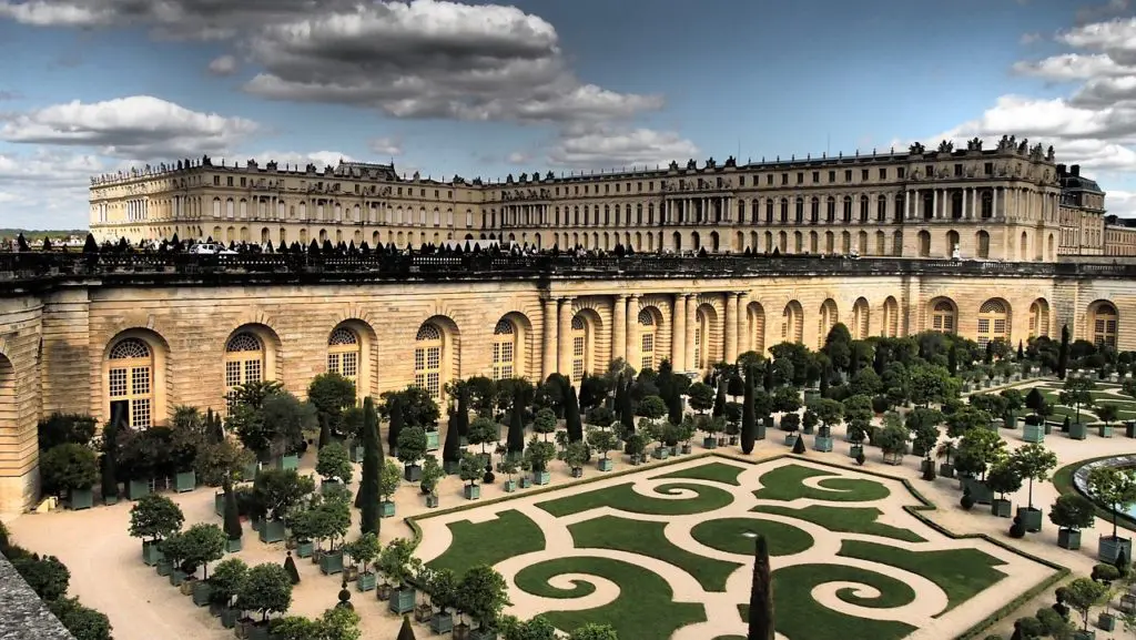 The grand rear facade of the Palace of Versailles towers over the formal Orangerie gardens and sculpted topiary below