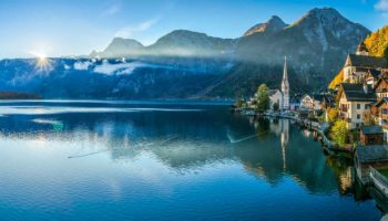 The village of Hallstatt on the shores of Hallstätter See in the Austrian Alps at sunrise, with autumn foliage and mountain reflections in the calm lake