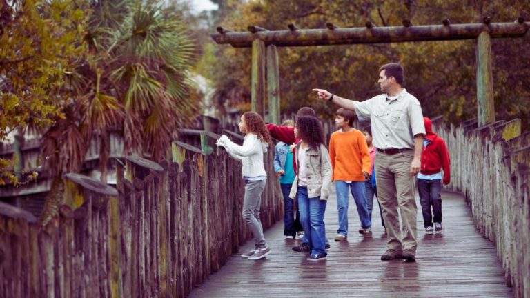 A teacher on a boardwalk, walking with his students teaching them on this class trip.