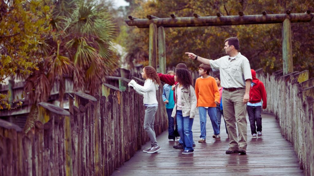 A teacher on a boardwalk, walking with his students teaching them on this class trip.